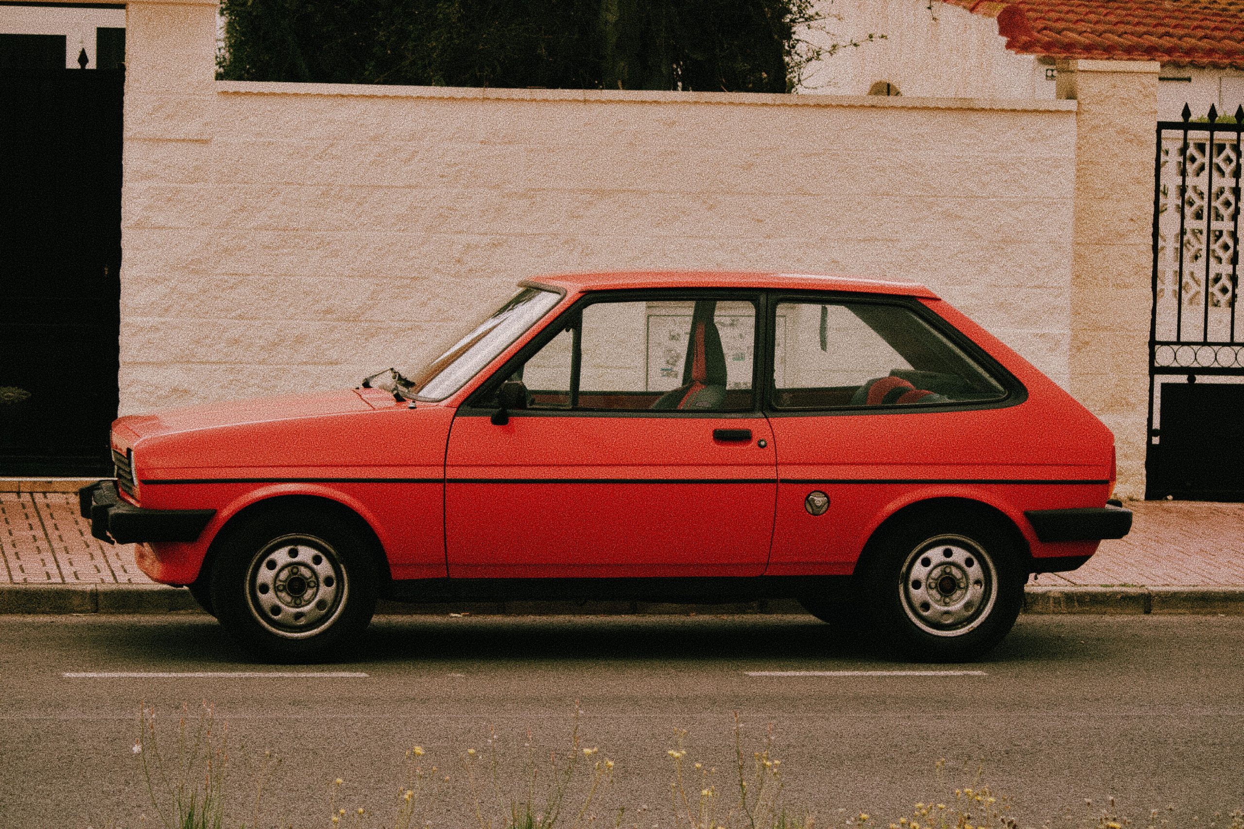 Clio rouge classique devant mur pierre blanche.